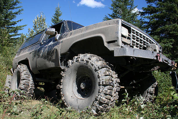 Big 4x4 truck with 44 inch tires, parked in the forest, covered in mud.